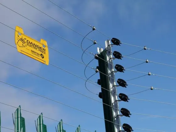 Electric fence post with insulators and live wires, and a danger sign, against a blue sky