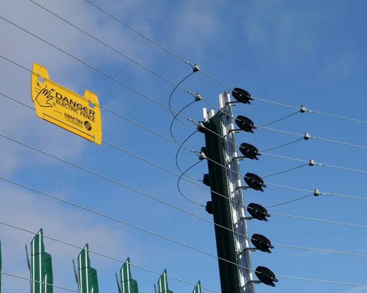 Electric fence post with insulators and live wires, and a danger sign, against a blue sky